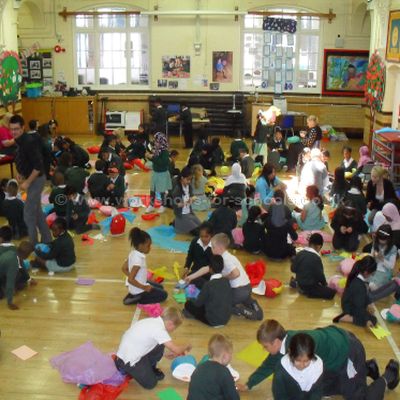 A large group of children and adults making puppets in a school hall